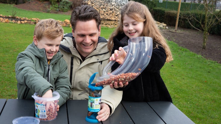 A father and two children fill up a blue bird feeder